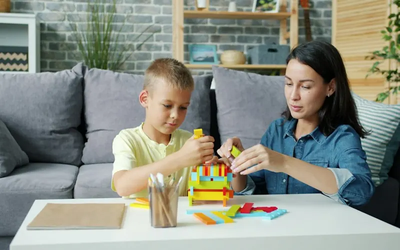Niña armando una torre de bloques de colores junto a una terapeuta